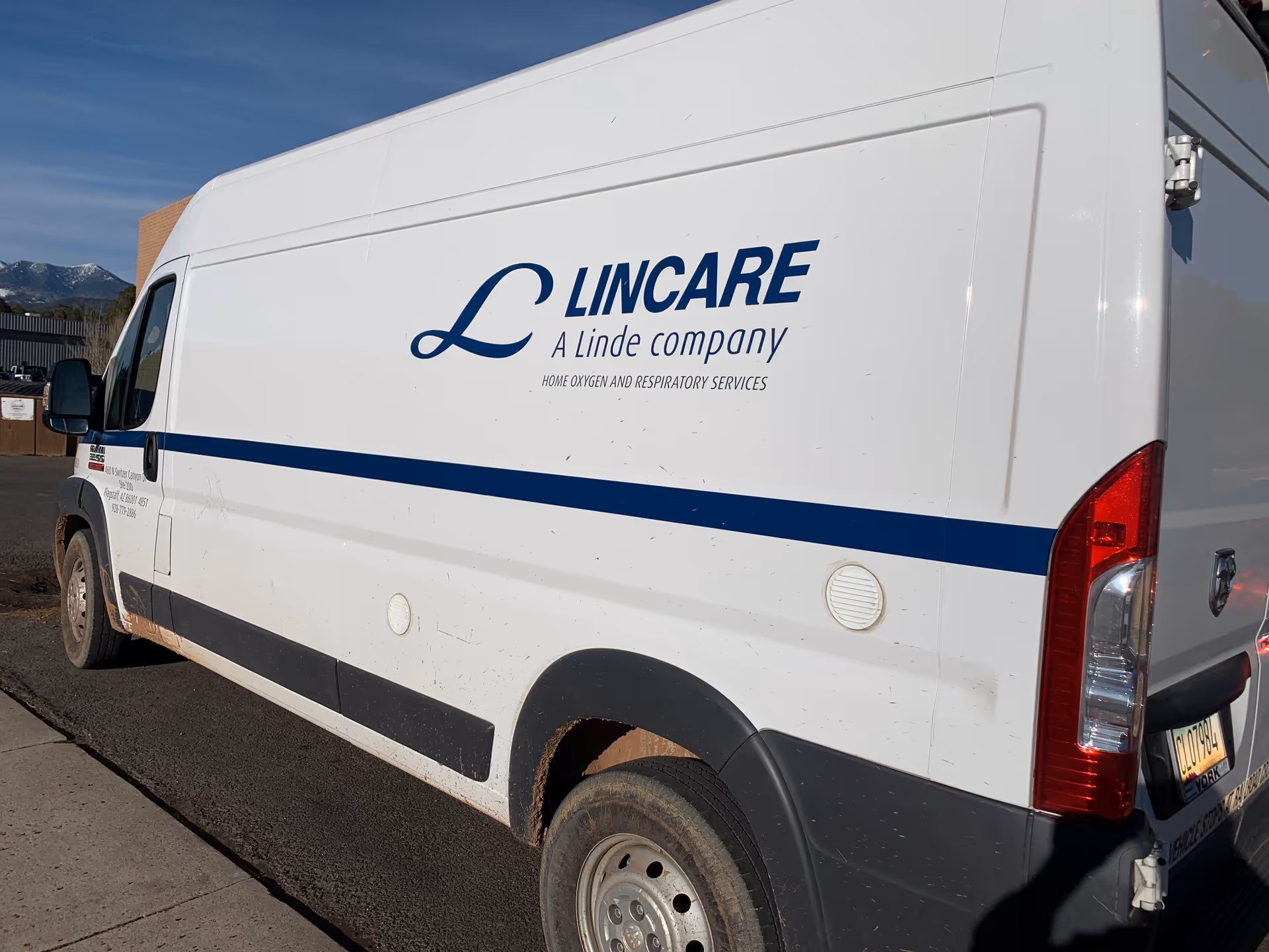 White Lincare van with blue stripe and logo parked outdoors.