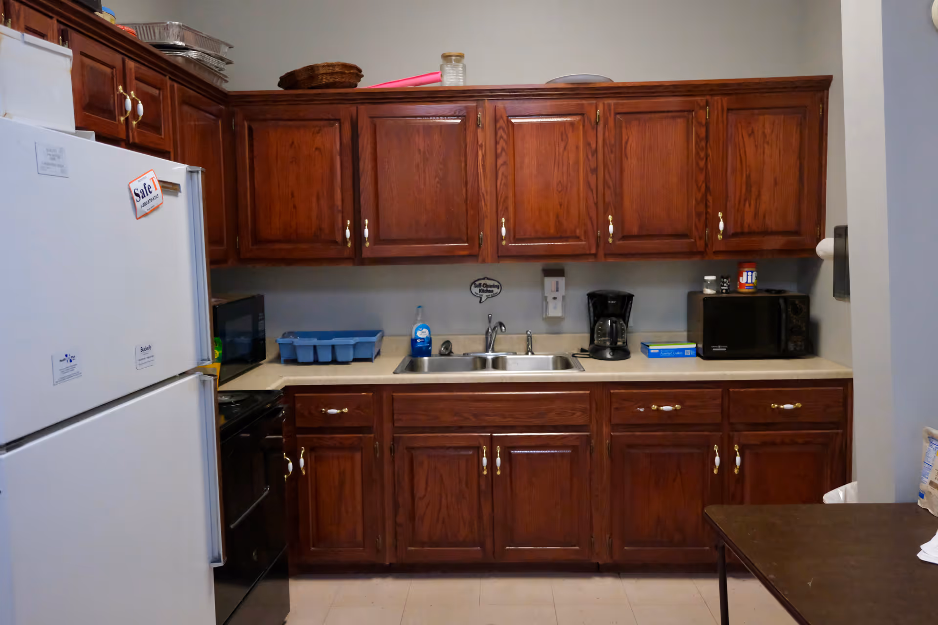 Wooden kitchen cabinets with fridge, sink, and appliances in a compact senior living kitchenette.