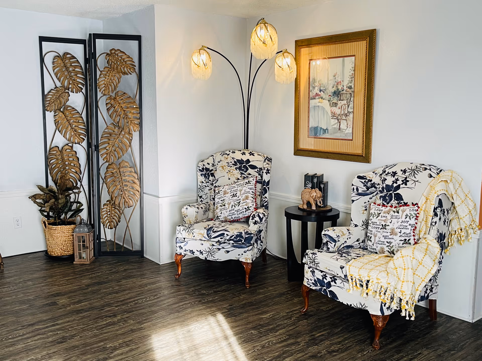 Two floral armchairs with a side table, lamp, and decorative screen in a cozy living room.