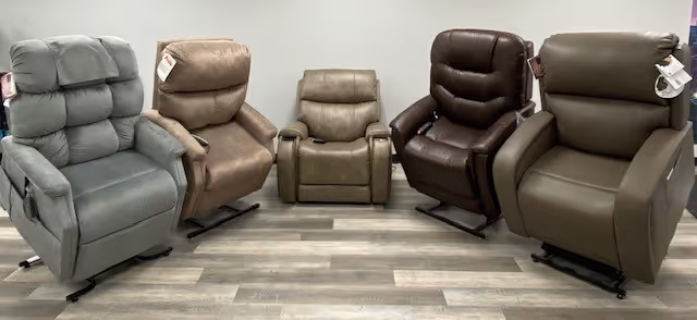 Five reclining chairs in gray, tan, and brown arranged in a showroom on wooden flooring.