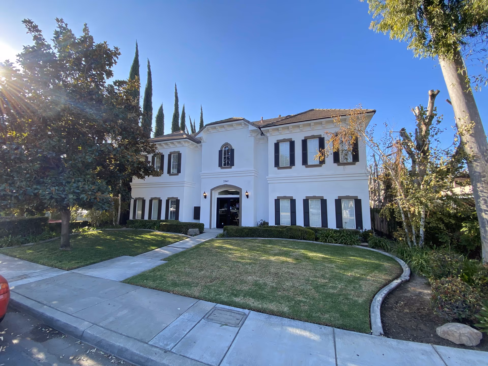 White two-story building with black shutters and a manicured lawn, front entrance.