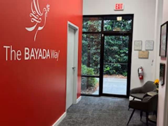 Red wall with The BAYADA Way logo, glass entrance doors, and seating inside lobby.