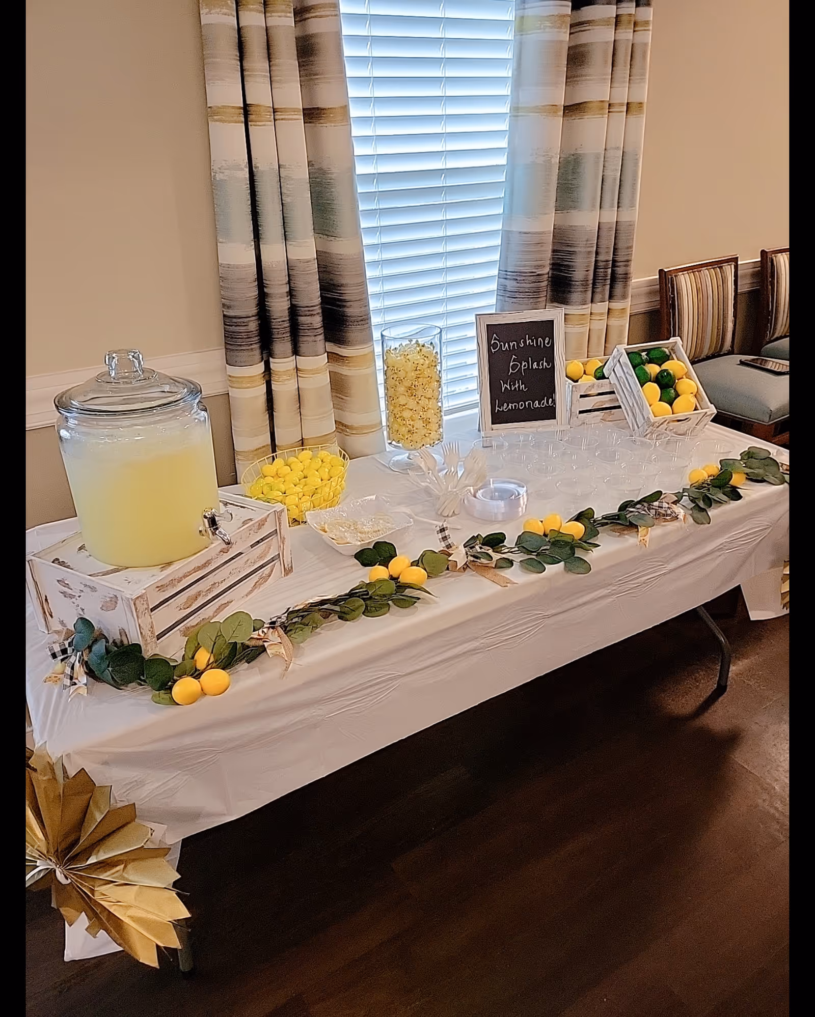 Lemonade station on a white-draped table with jars, lemons, and a chalkboard sign.