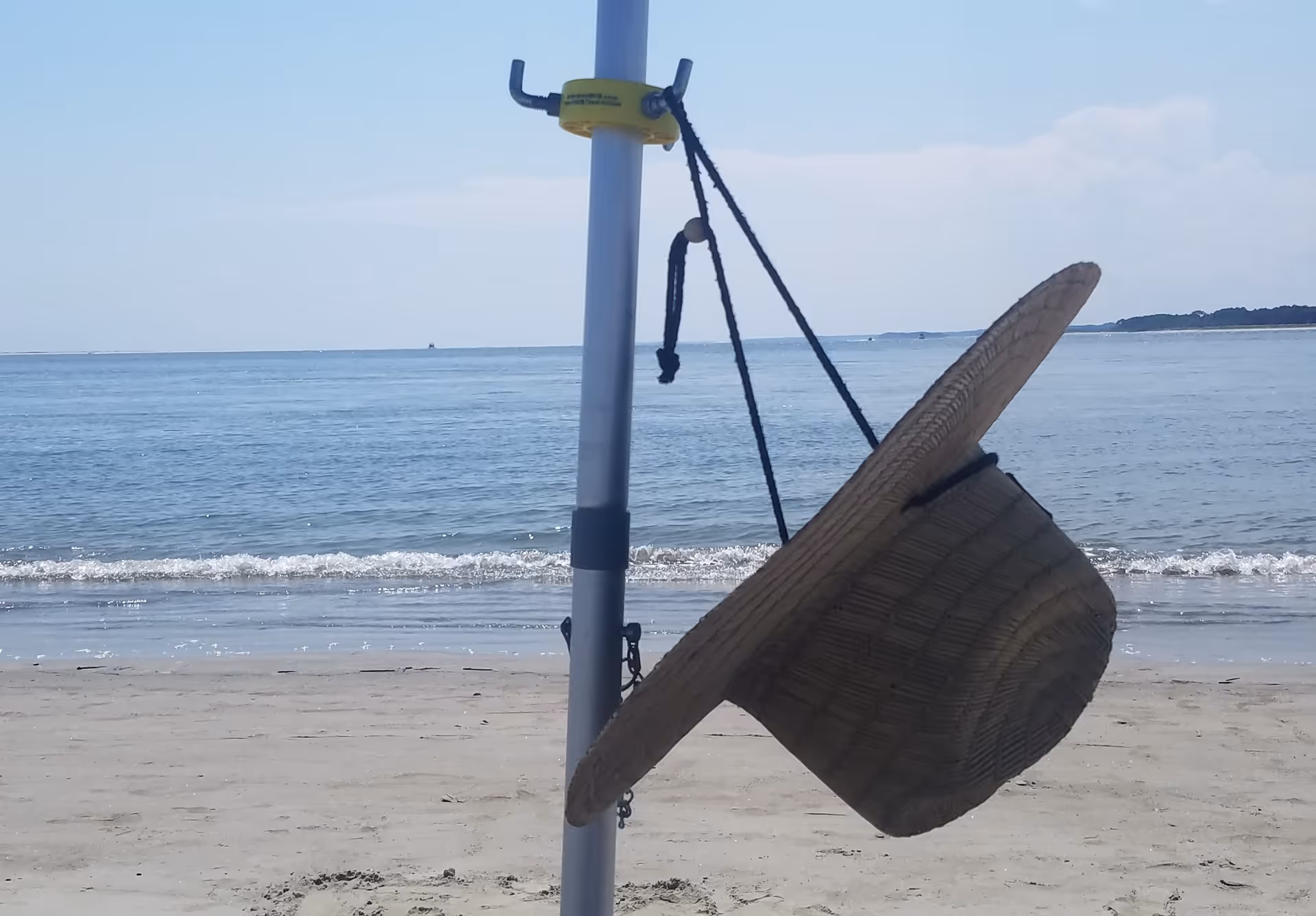 Wicker hanging chair attached to a pole on a sandy beach by the water.