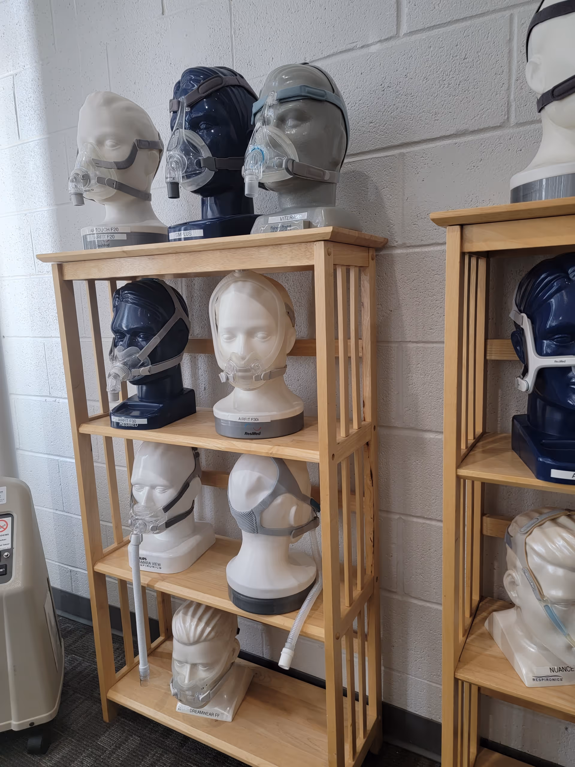 Wooden shelves display CPAP masks and mannequin heads along a white brick wall.