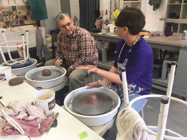 Two seniors work at pottery wheels in a craft room, shaping clay together.