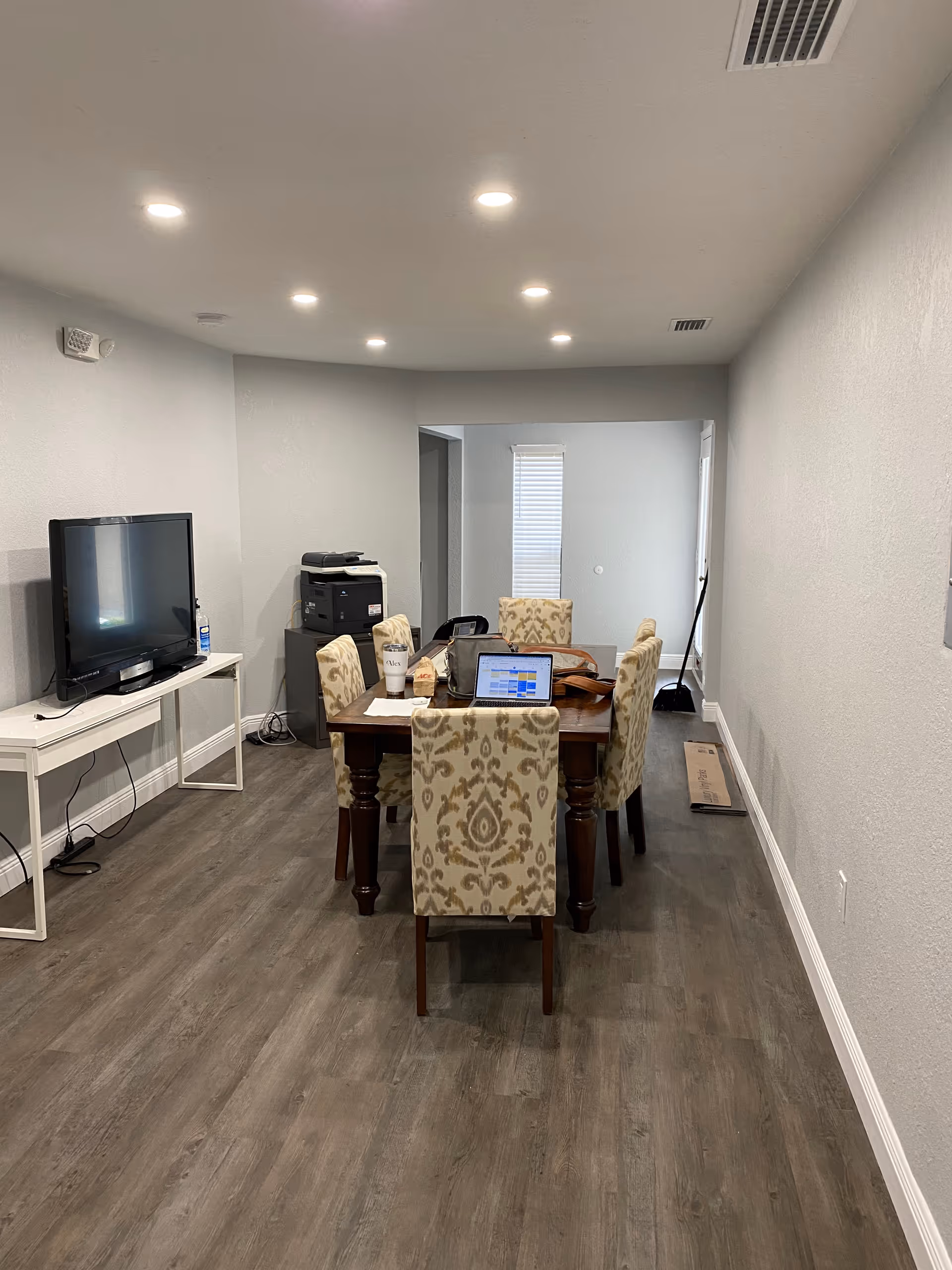 A dining area in a senior facility with a table, upholstered chairs, laptop, and TV.