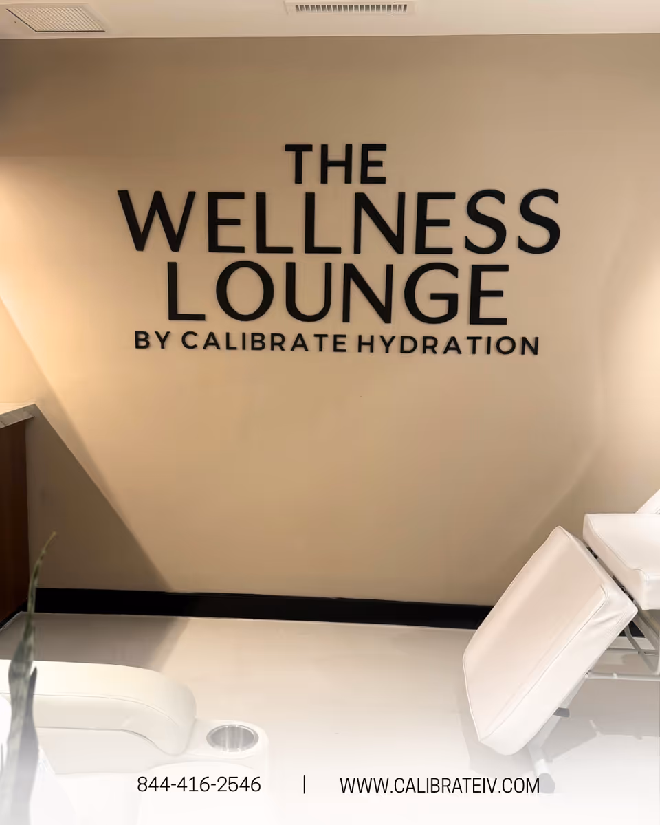 Interior wall with large sign reading The Wellness Lounge by Calibrate Hydration and white lounge chairs