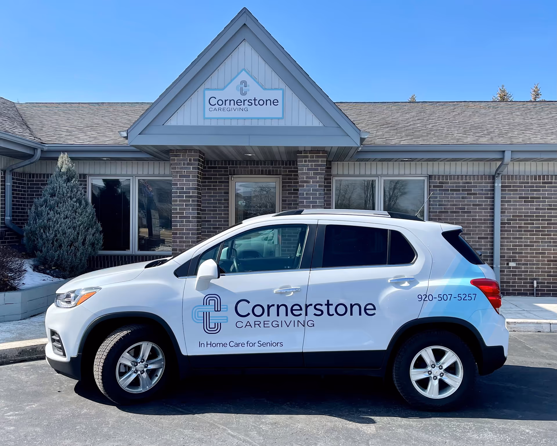 A white Cornerstone Caregiving SUV parked outside a brick Cornerstone facility.