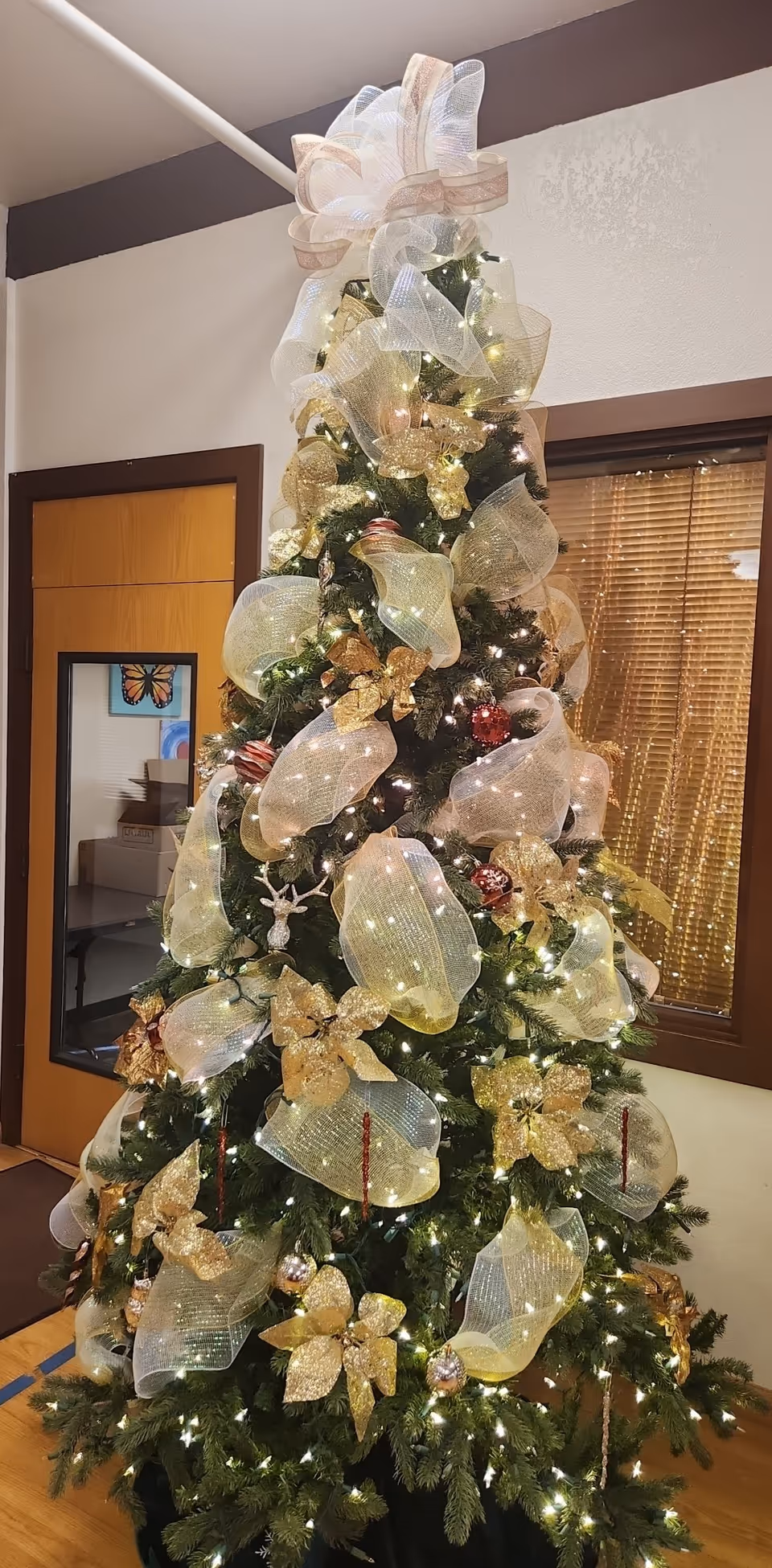 Decorated Christmas tree with gold ribbons and white lights in an indoor facility lobby.