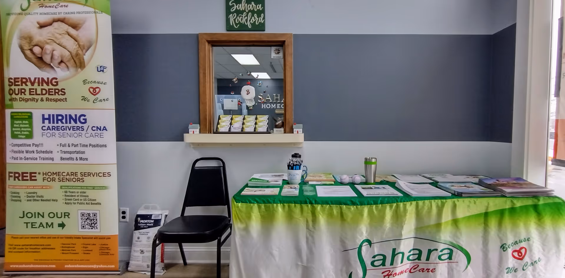 Indoor reception area with a green-covered table, brochures, a chair, and signage.