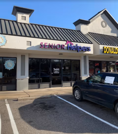 Exterior view of a Senior Helpers storefront with a purple sign in a strip mall.