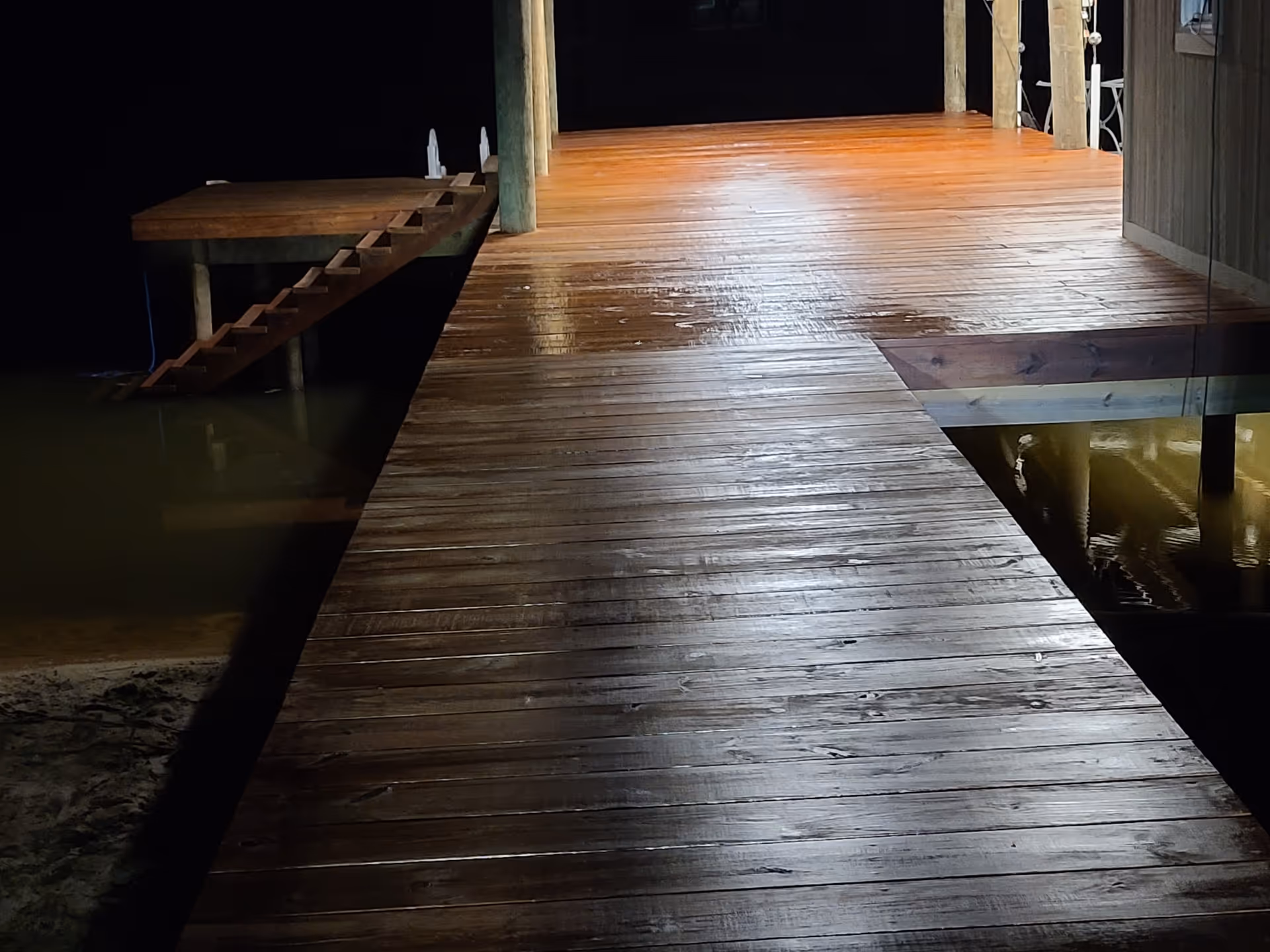 Dimly lit wooden dock extends over calm water at night.