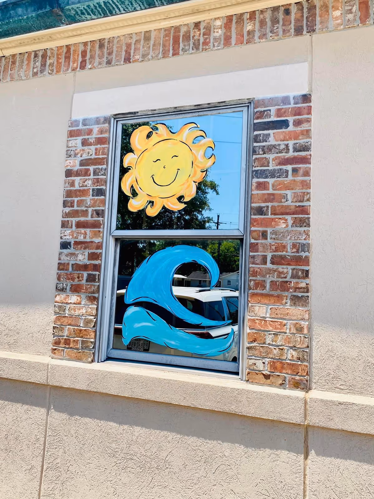 Brick exterior wall featuring a window mural of a smiling sun and blue wave.
