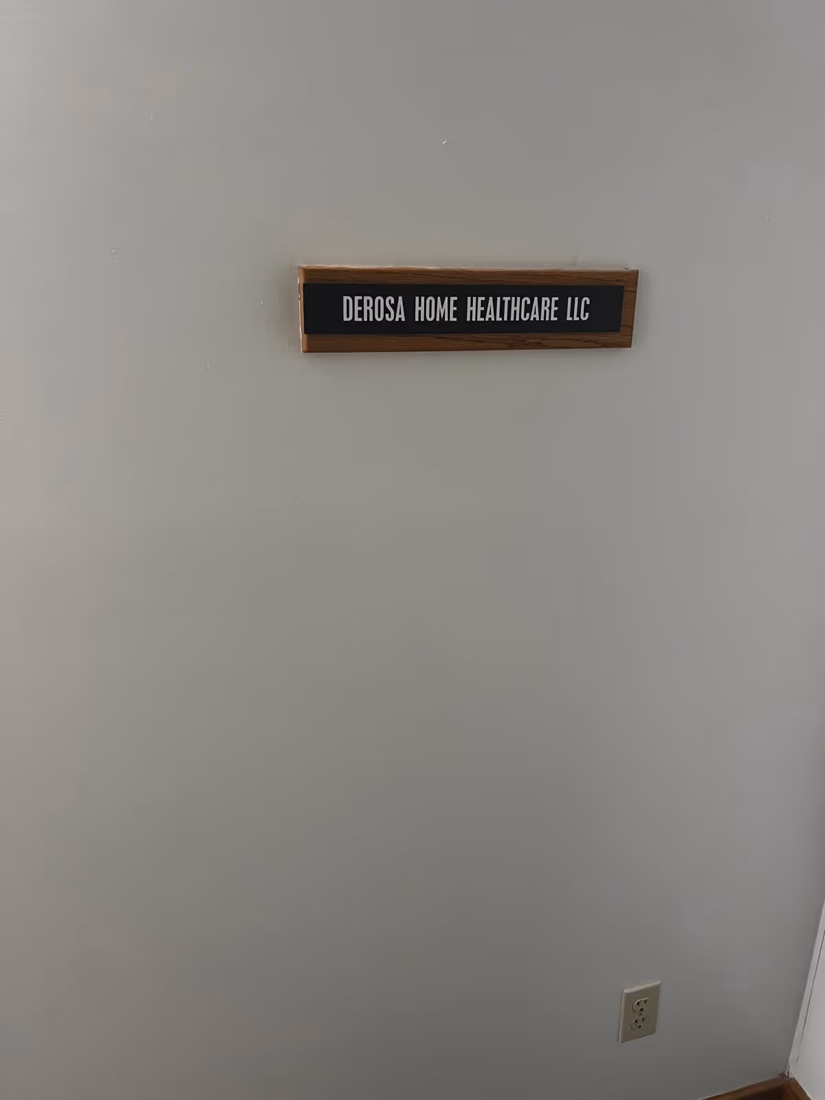 Plain interior wall with a wooden plaque reading DeRosa Home Healthcare LLC.