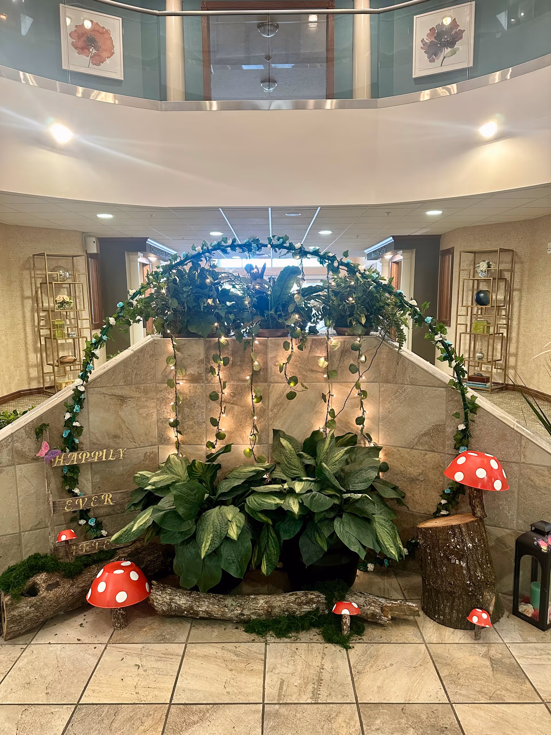 Indoor lobby atrium with leafy arch, hanging vines, potted plants, and red toadstool decorations.