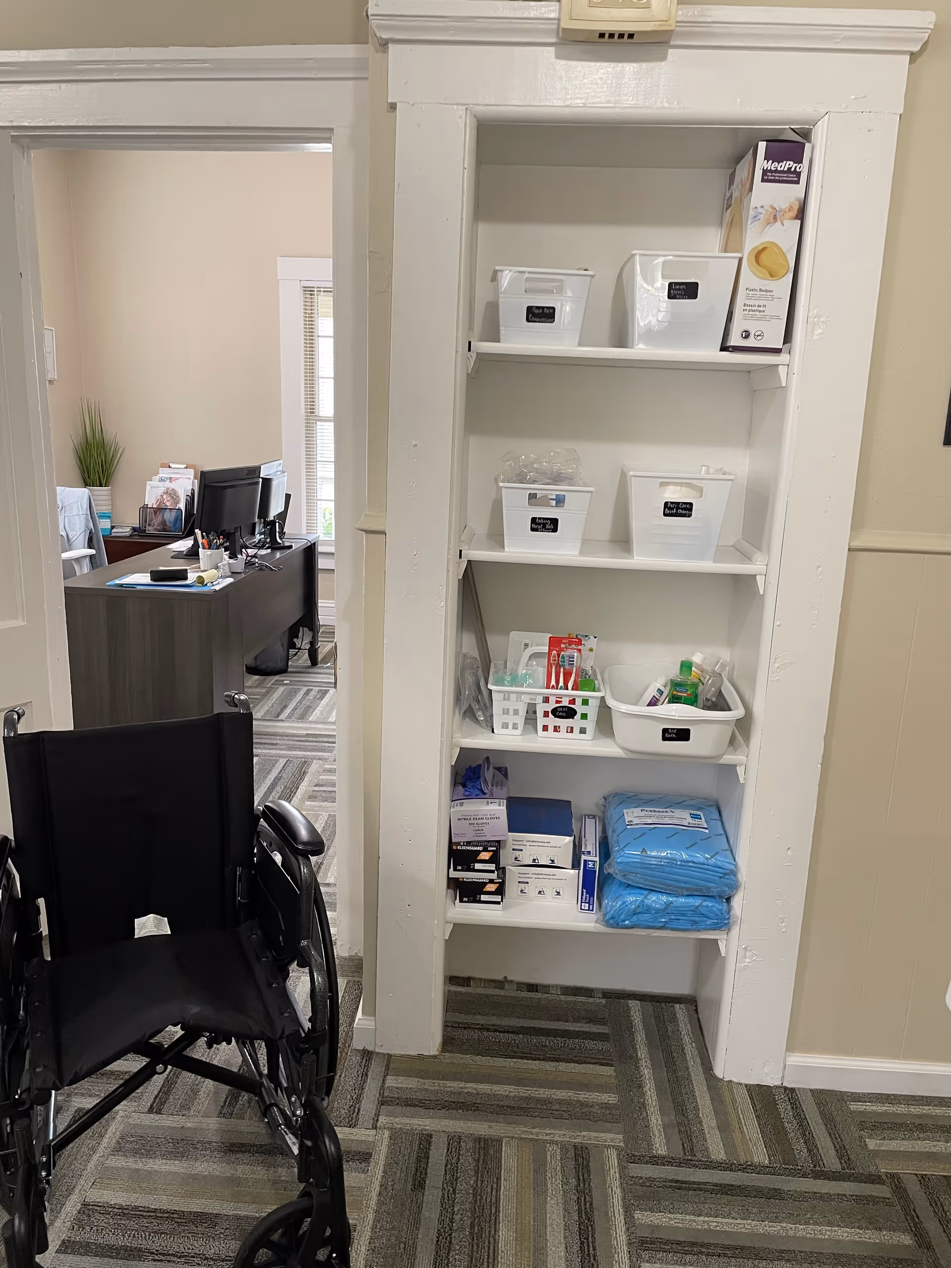 Wheelchair in a facility hallway beside a tall storage shelf with medical supplies.