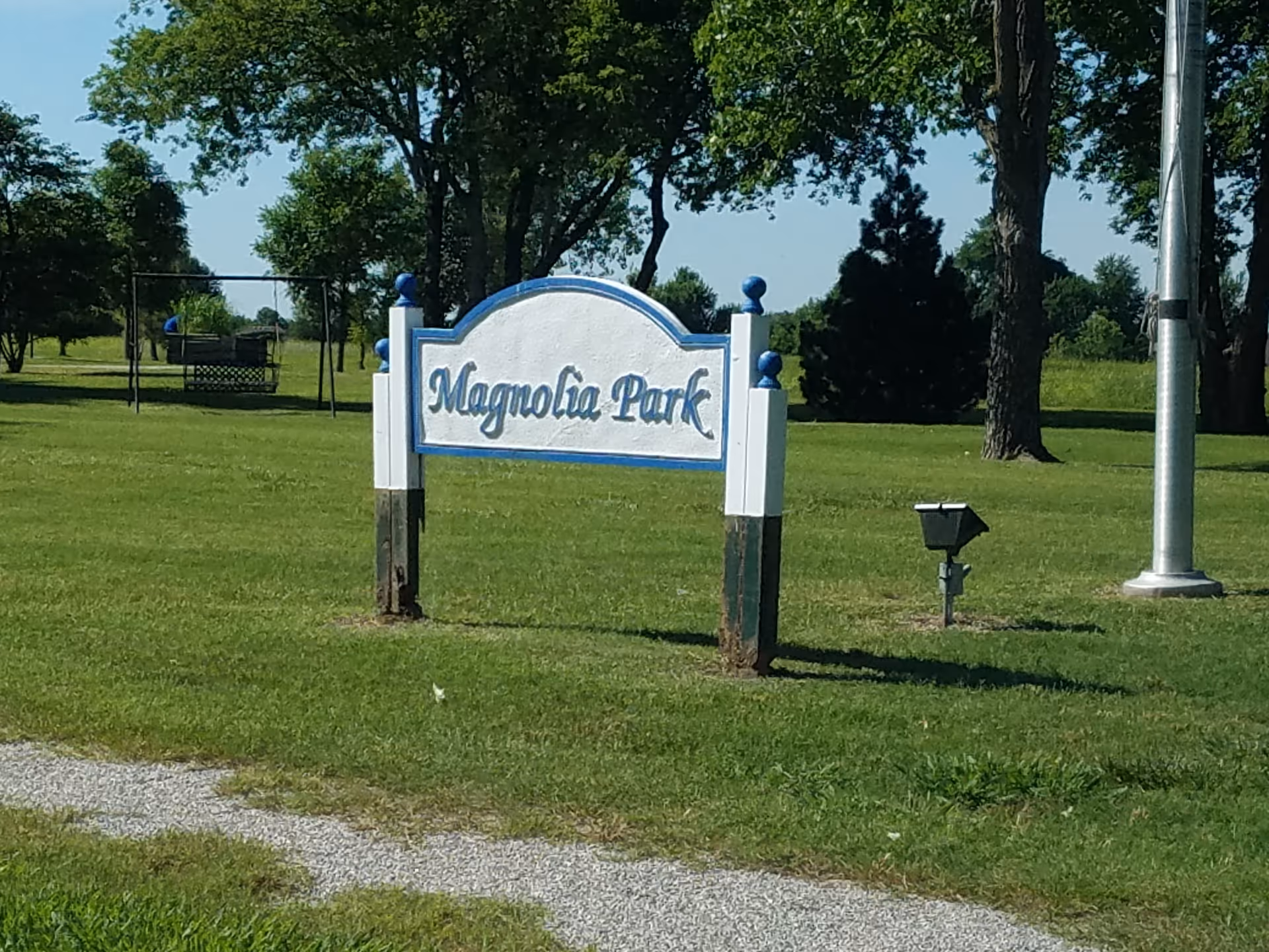 Magnolia Park sign on a grassy lawn with trees and a gravel path.
