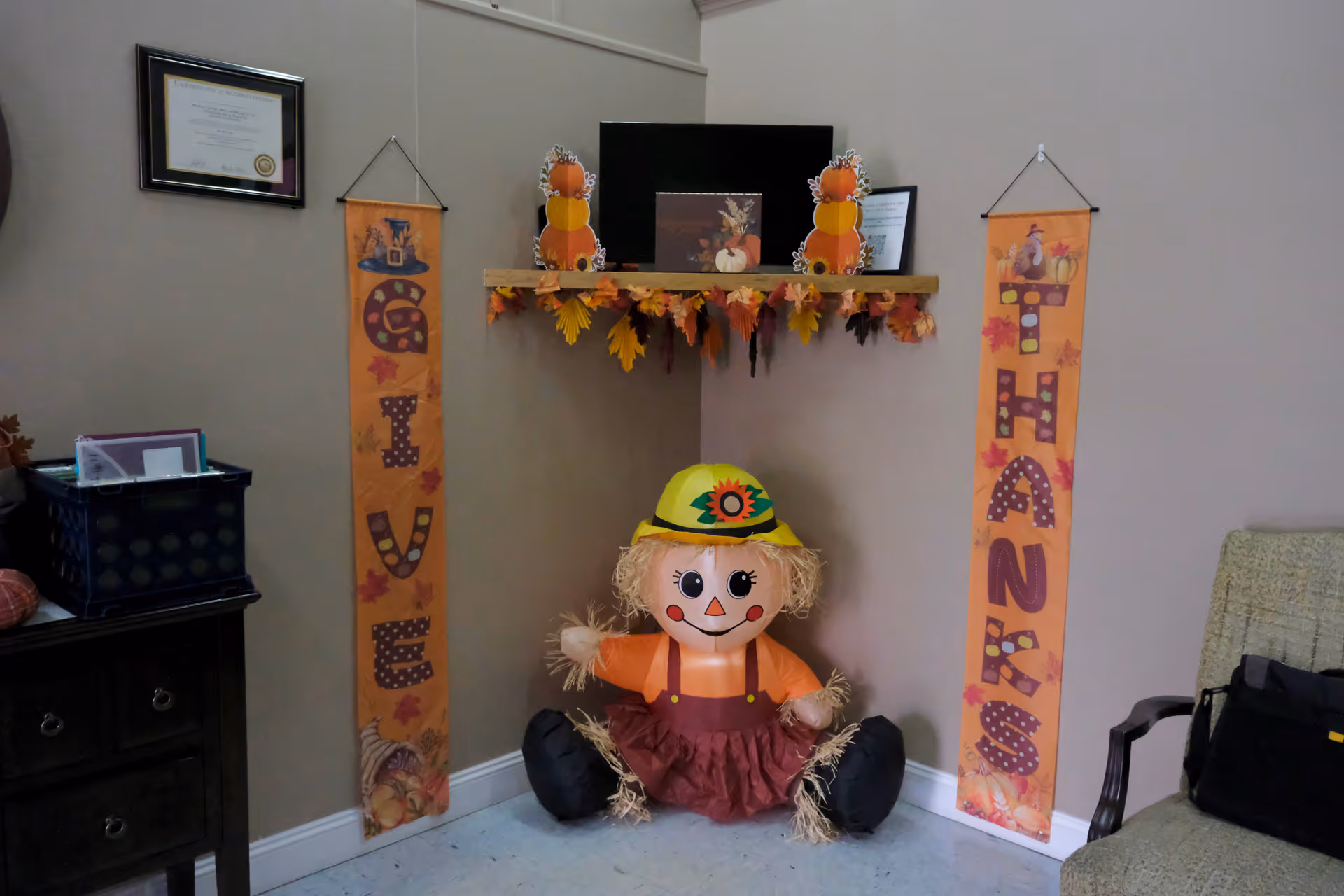 Autumn-themed corner in a room with banners, a scarecrow doll, and shelf decorations.