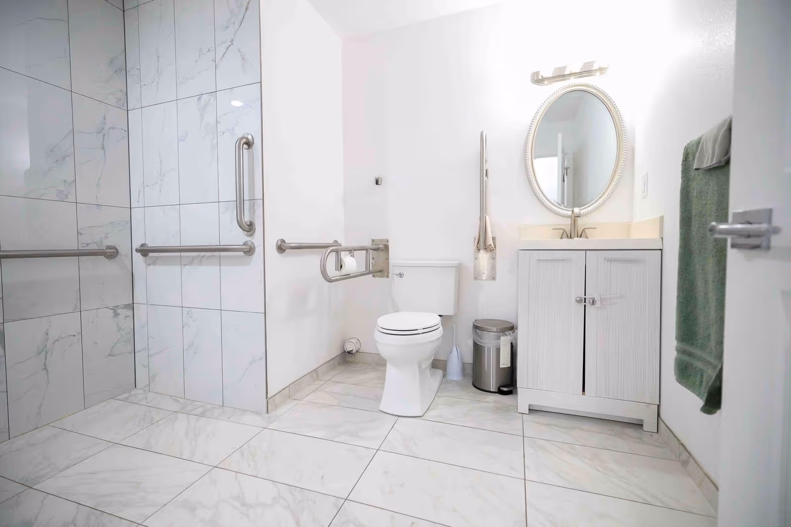 Bright accessible bathroom with toilet, sink, mirror, towels, and multiple grab bars.