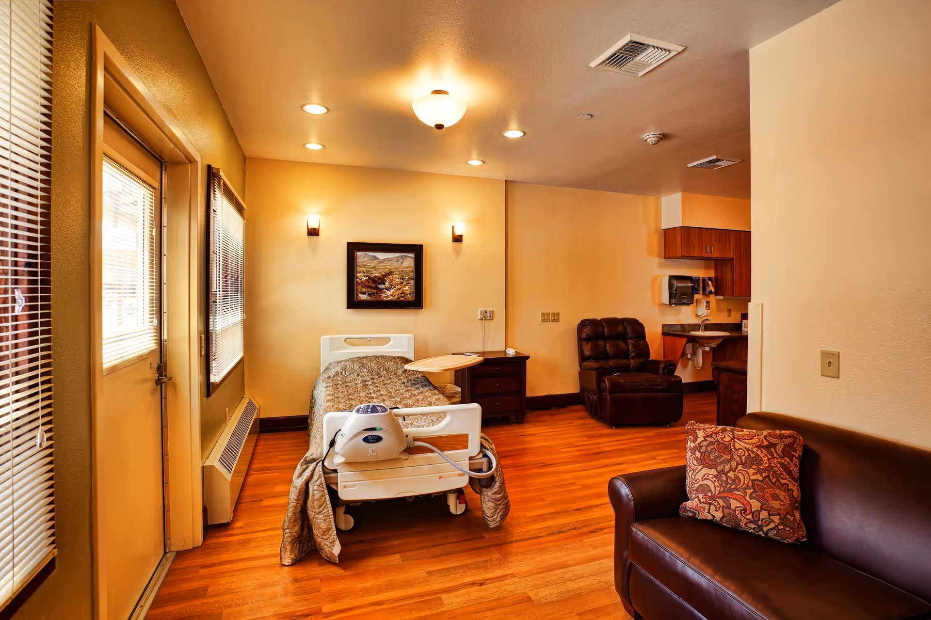 Hospice room features a bed, recliner, sofa, and small kitchenette.