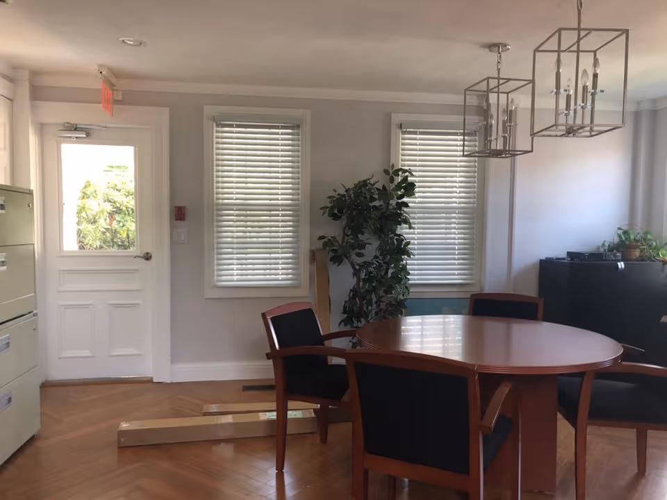Round wooden dining table with chairs in a bright, modern communal dining area.