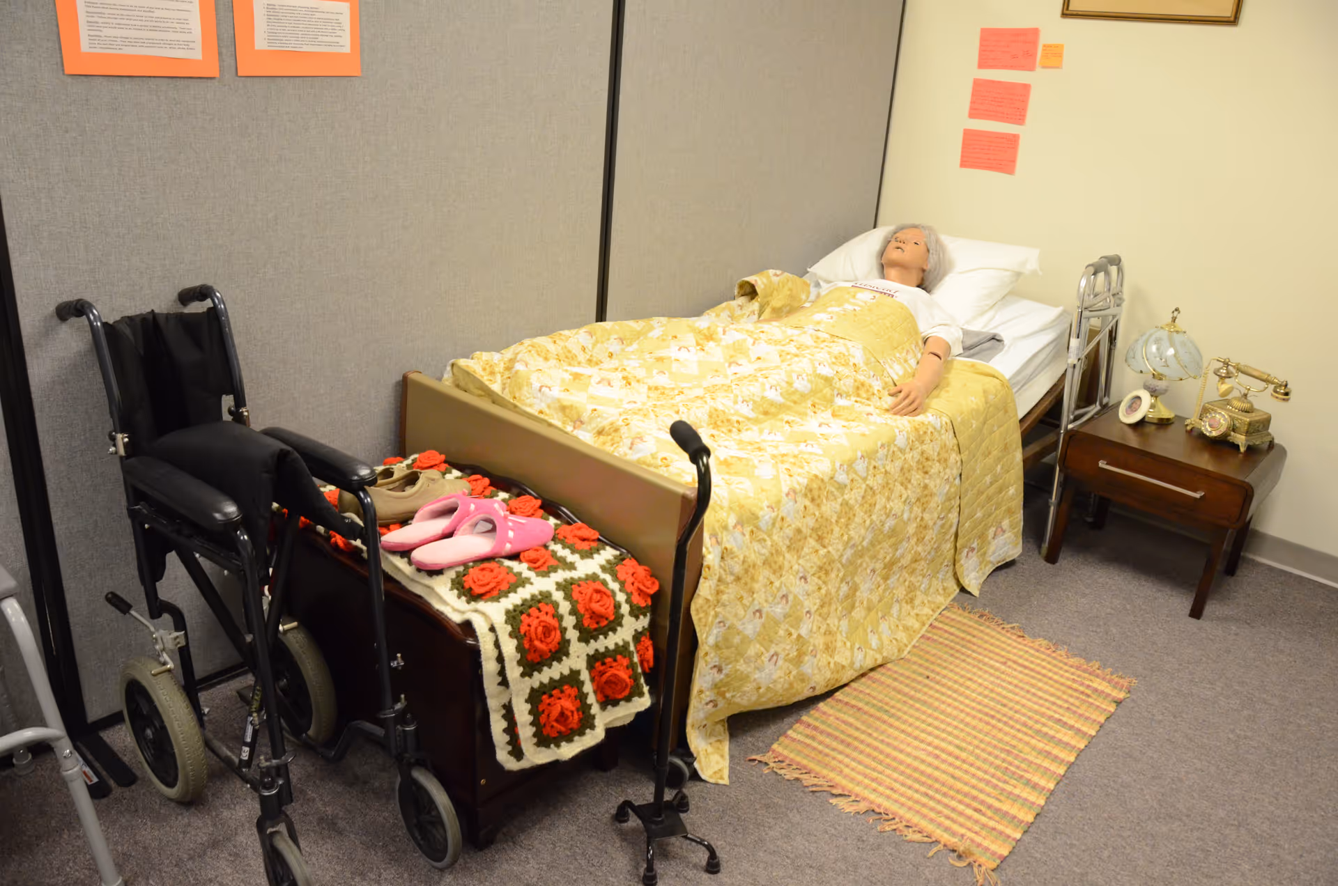 A care room with a bed, yellow quilt, walker, wheelchair, and side table.