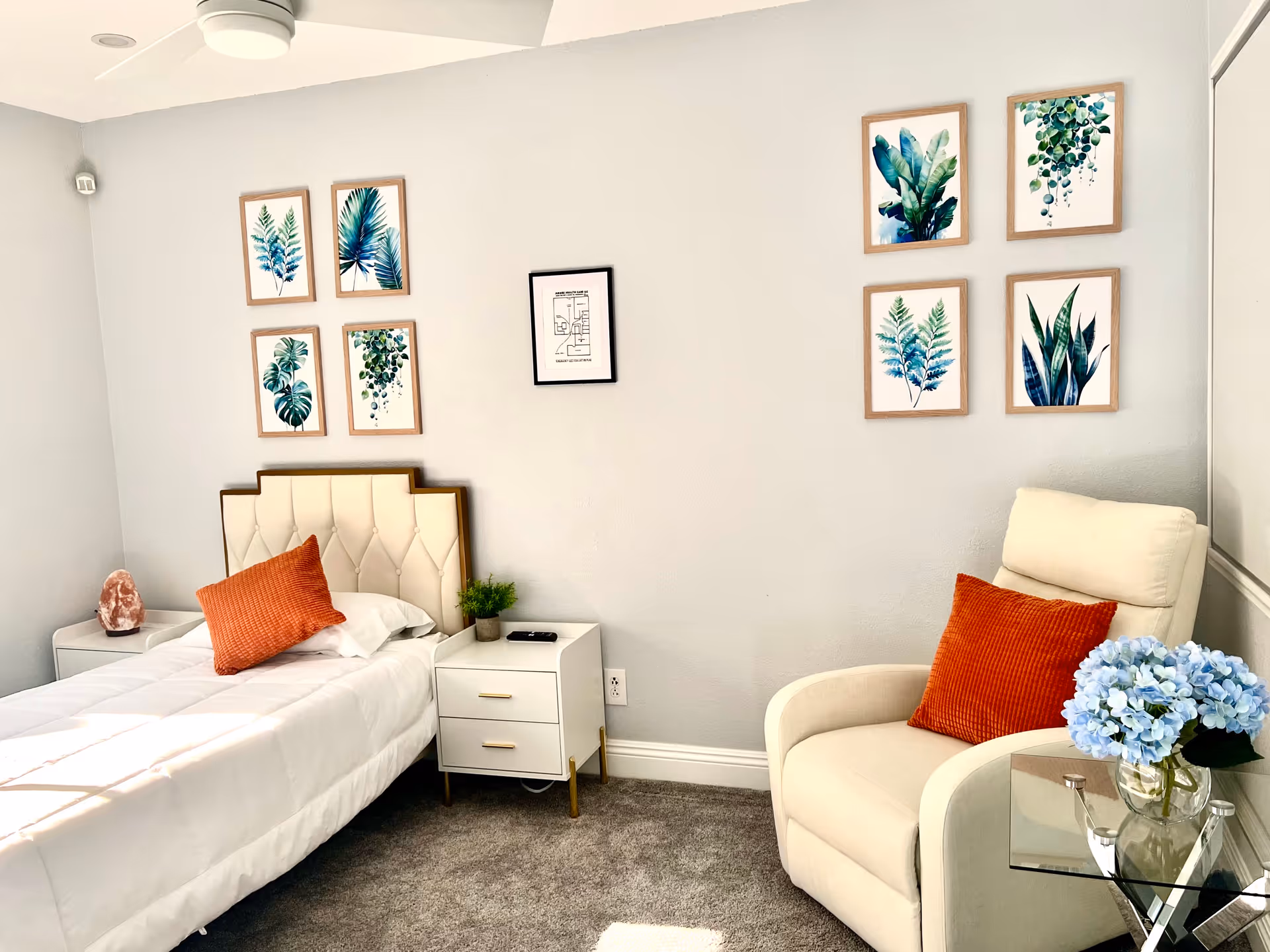 A tidy bedroom with a single bed, nightstands, seating area, and botanical wall art.