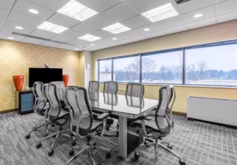 Empty conference room with a long table, office chairs, and large windows overlooking outdoors.
