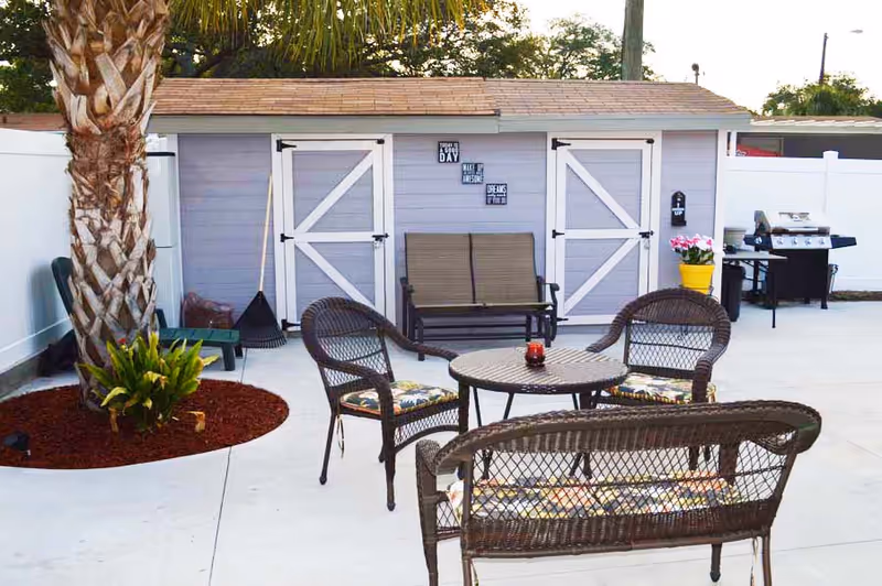 Outdoor patio with wicker seating, a round table, grill, and a small shed.