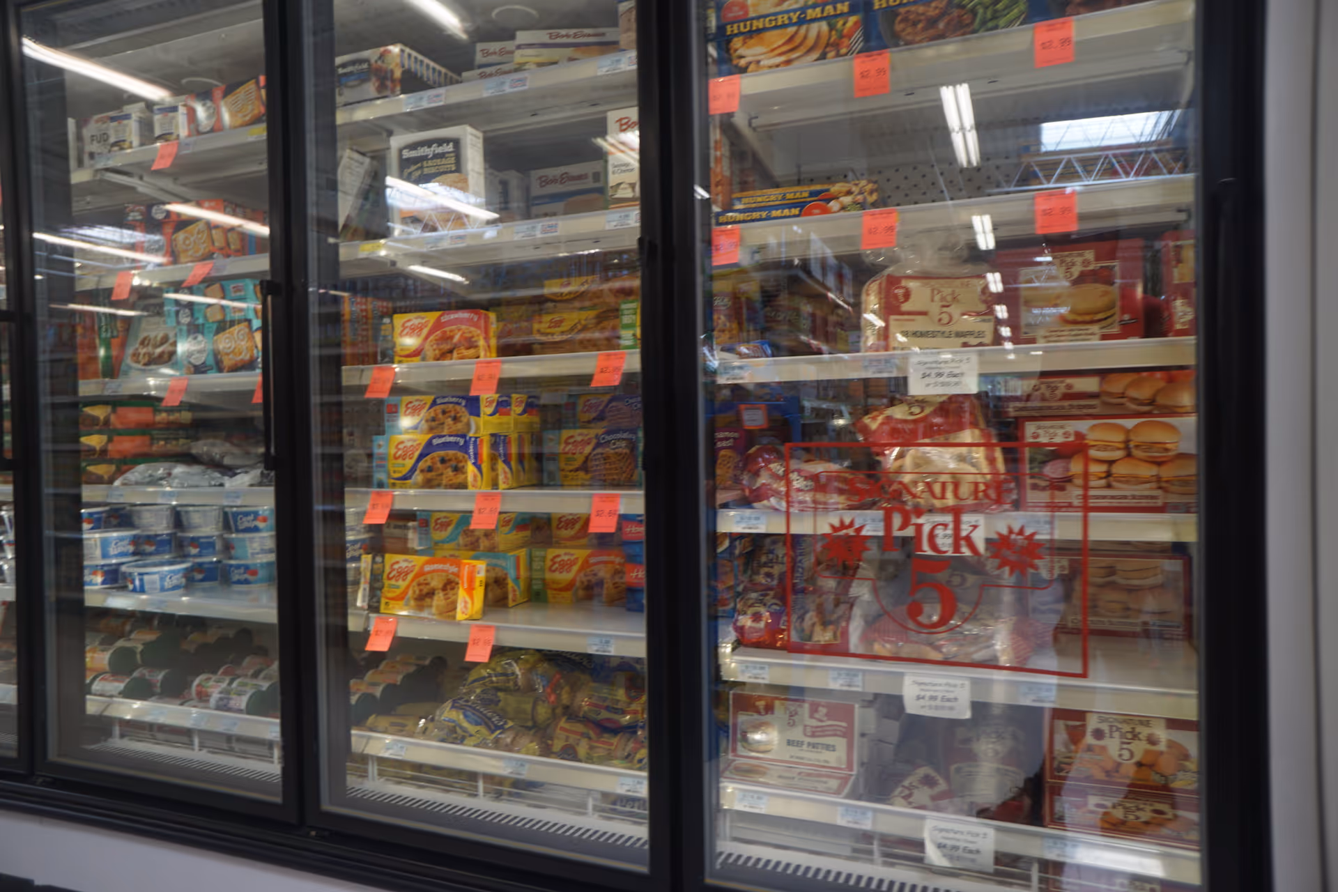 Interior view of refrigerated display cases with assorted frozen foods and sale tags.