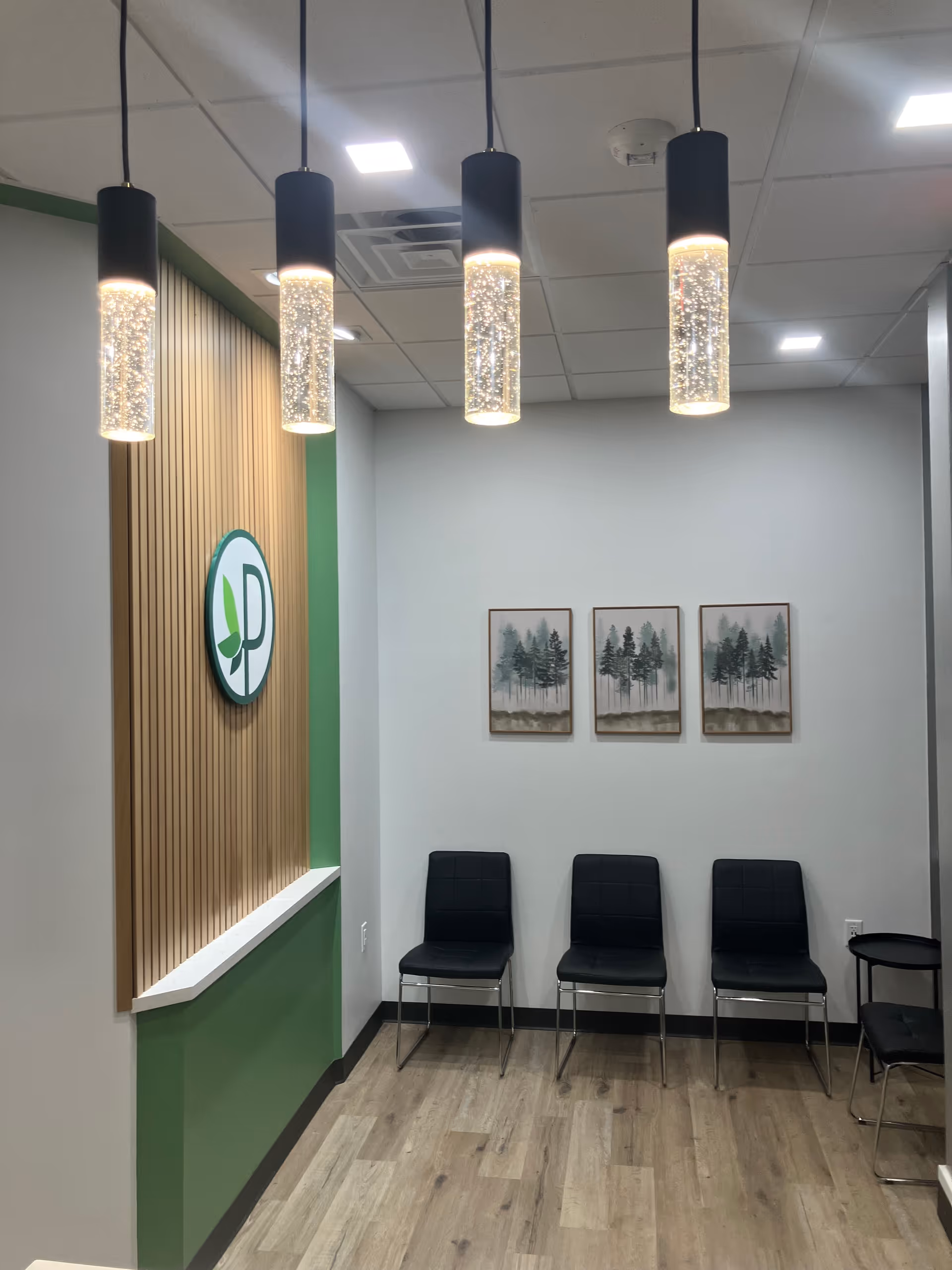 Lobby-like waiting area with green wall, wood slat wall accents, and four pendant lights.