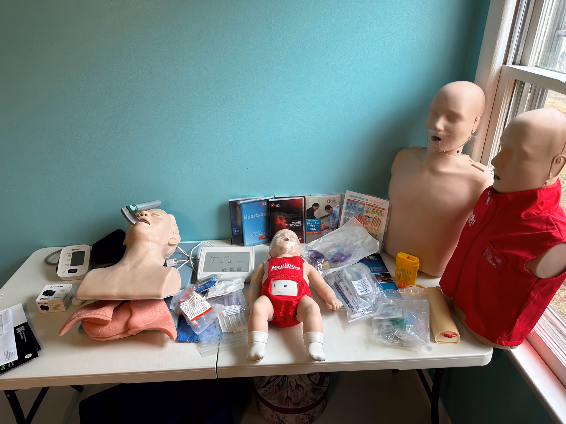 CPR training mannequins and medical supplies displayed on a table by a teal wall