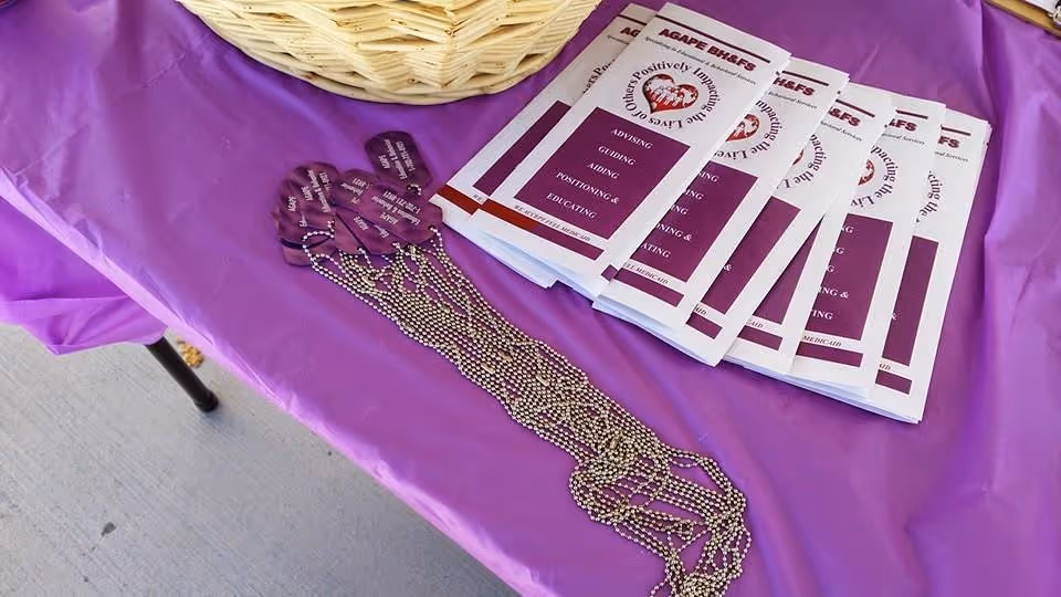 Purple table with AGAPE brochures, a basket, and beaded necklace on display.