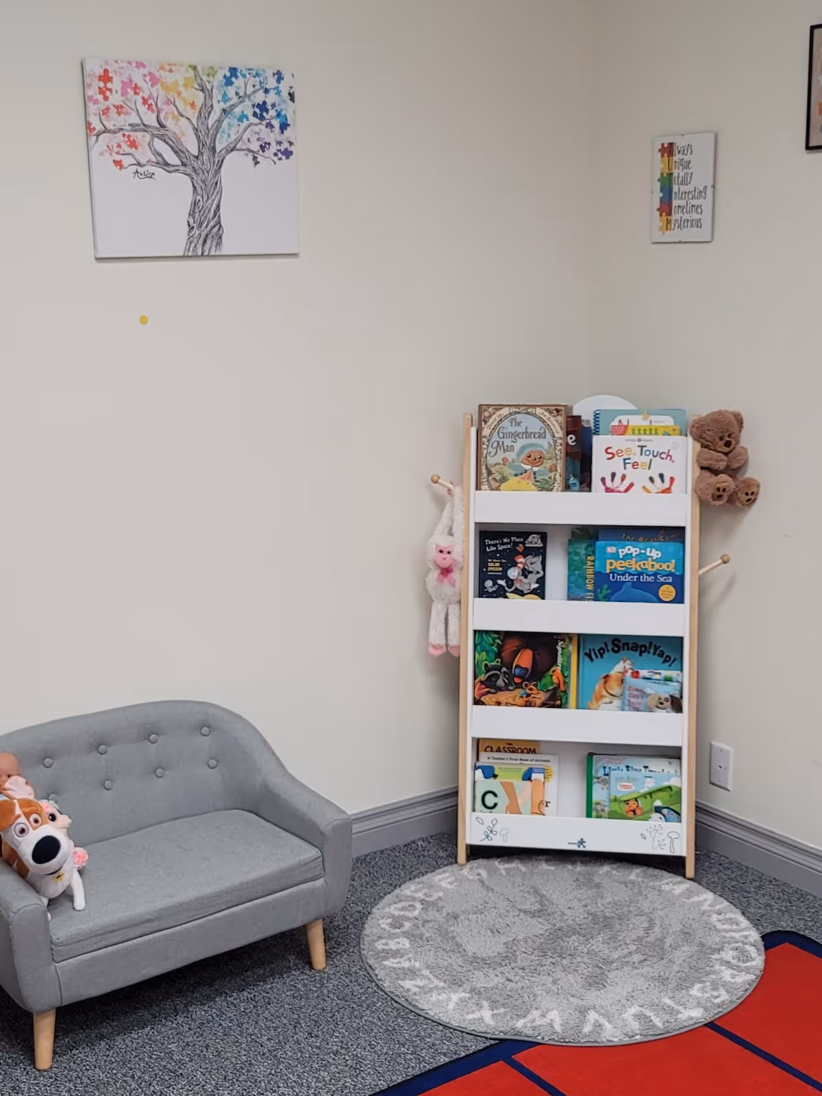 Small gray sofa beside a white bookshelf with stuffed animals and children's books.