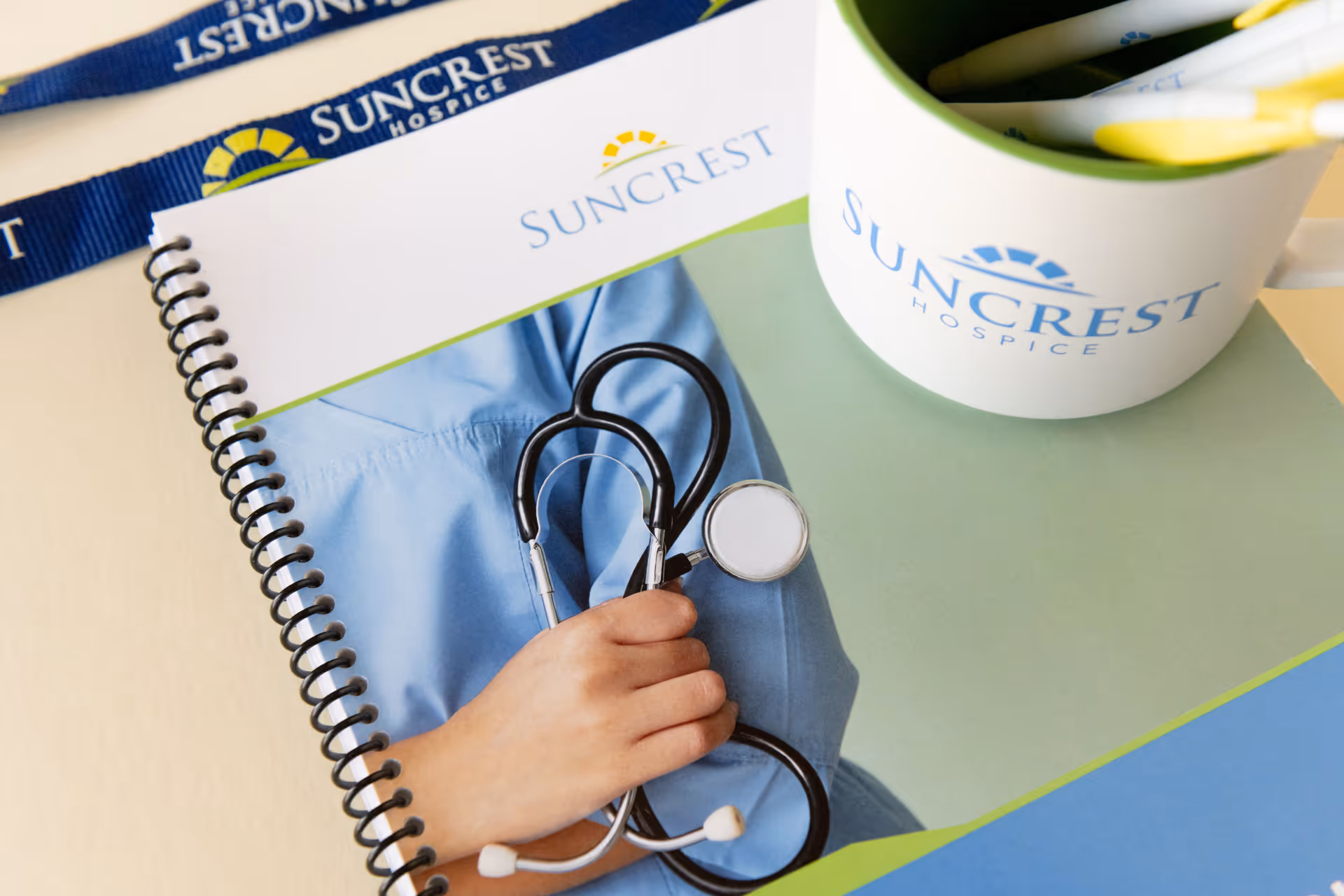 Close-up of a Suncrest Hospice stethoscope, notebook, and branded mug on a desk.