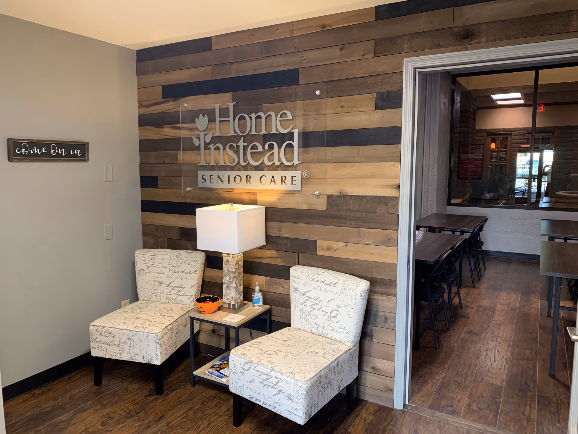 Interior lobby area with wood accent wall, Home Instead Senior Care sign, chairs, and doorway.