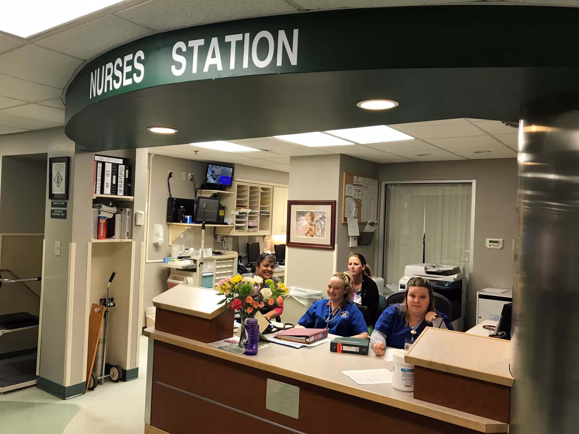 Interior nurses' station with four staff members seated at a curved front desk.