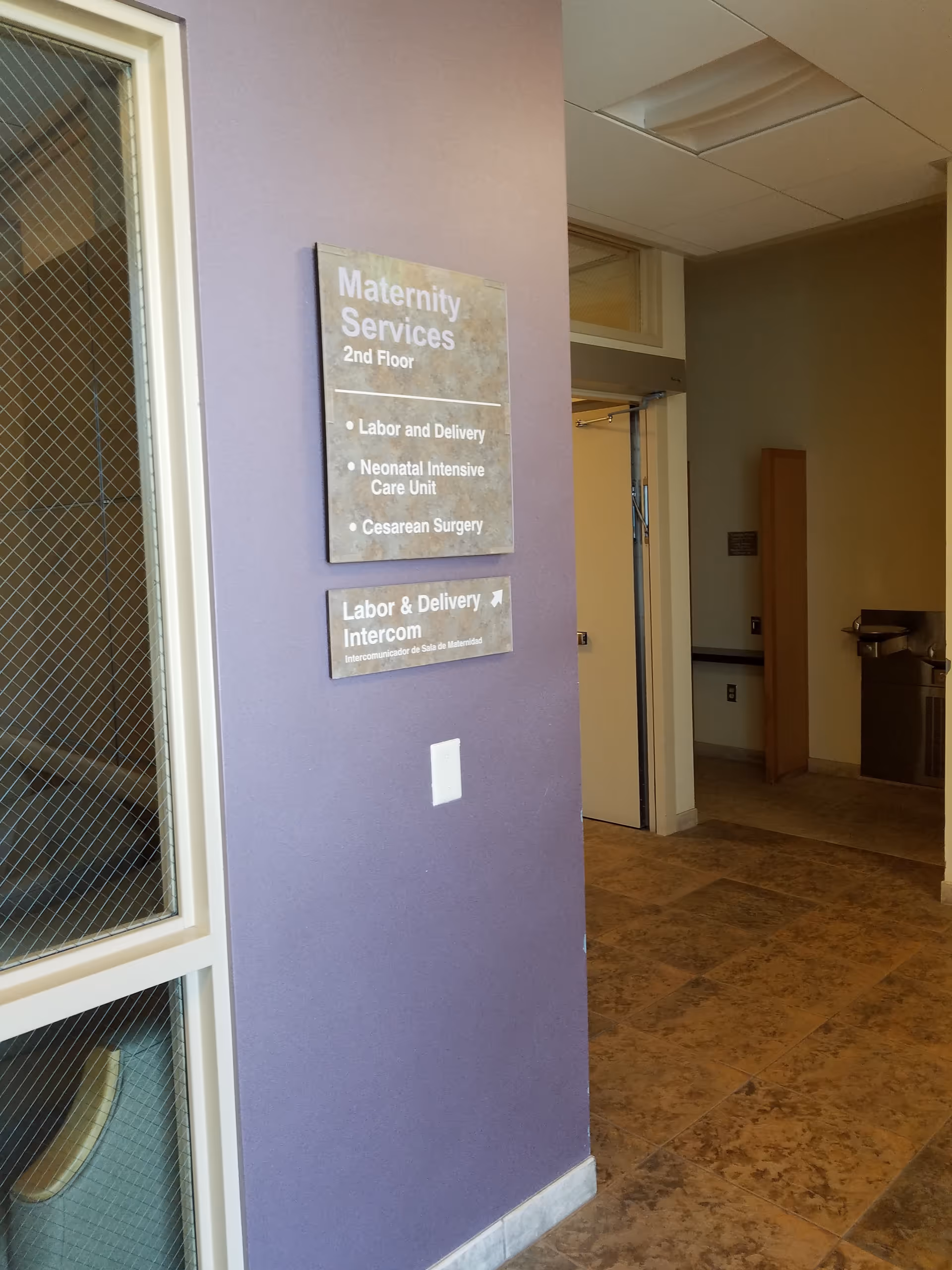 Interior hospital corridor with purple wall and maternity services signage.