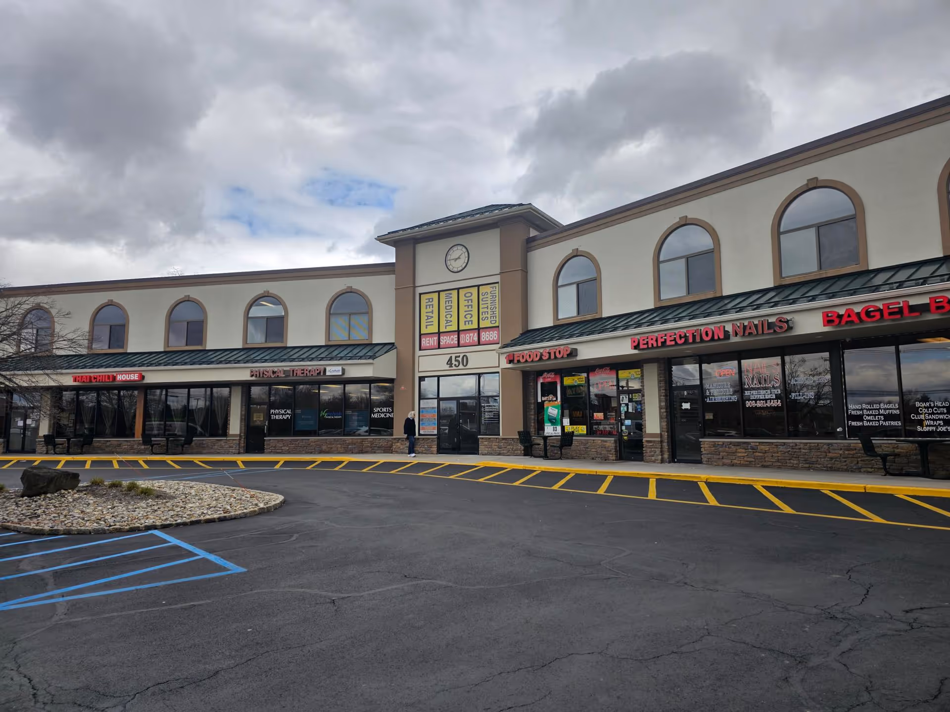 Exterior of a shopping plaza with several storefronts and a front parking lot.