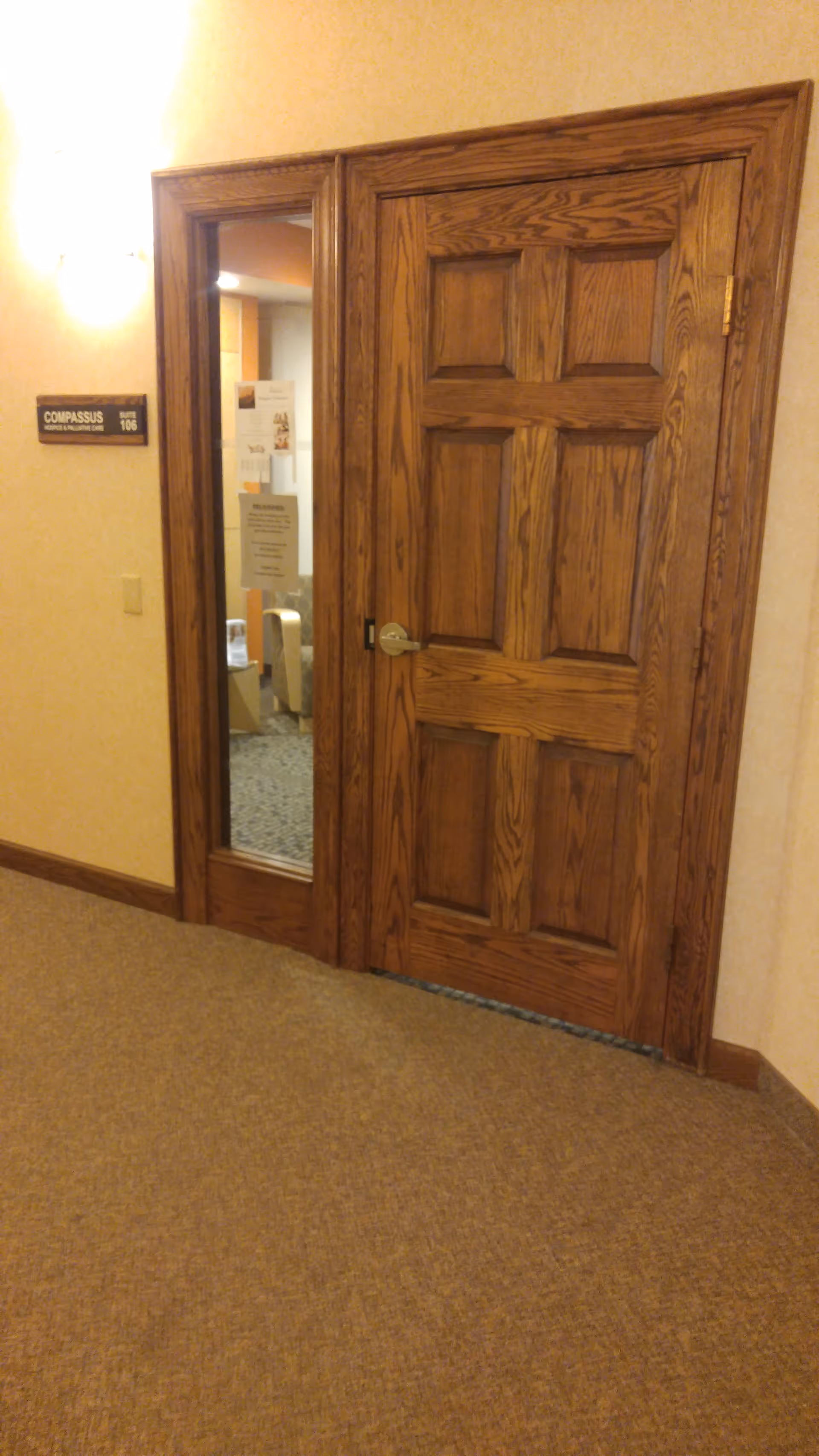 Wooden door with a glass panel beside a beige facility corridor.
