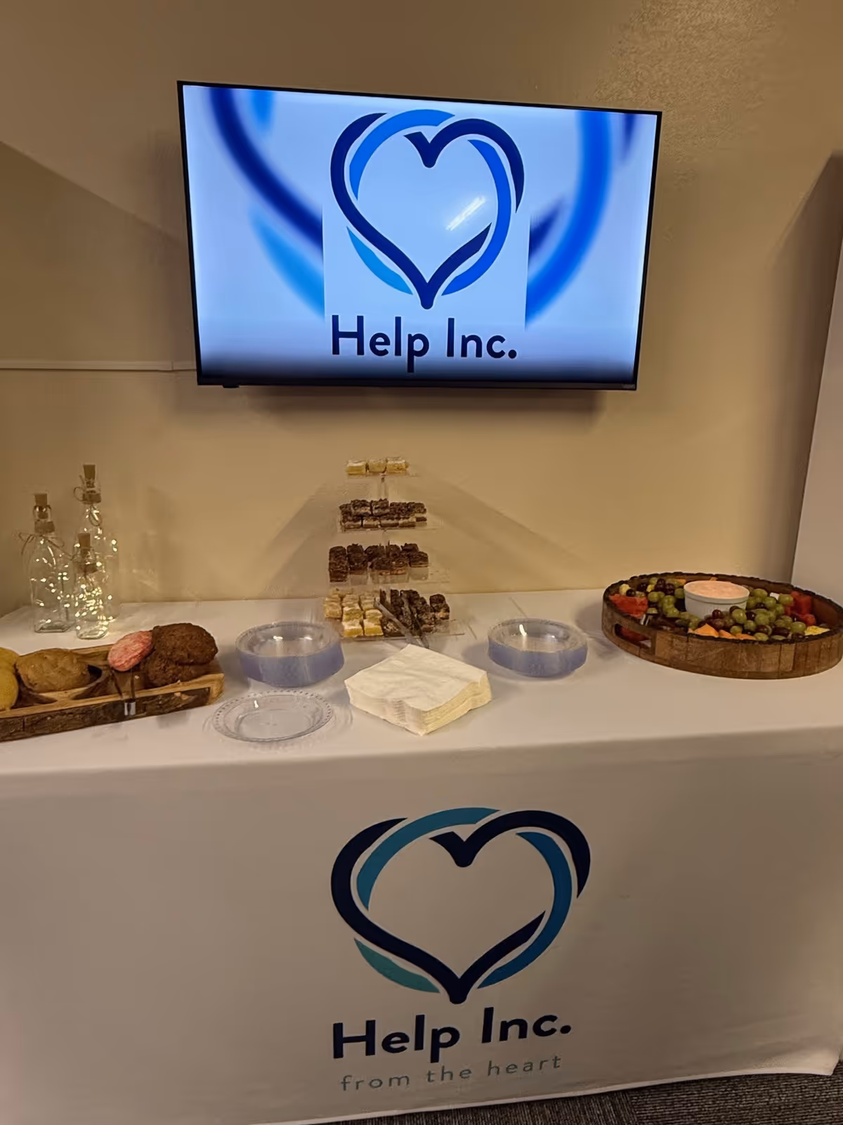 Display table with Help Inc. logo, monitor, and assorted desserts inside.