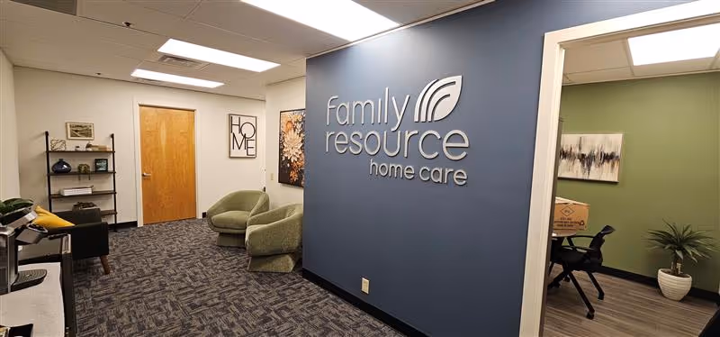Interior lobby area with blue wall logo, seating, and doorway in a senior care facility.