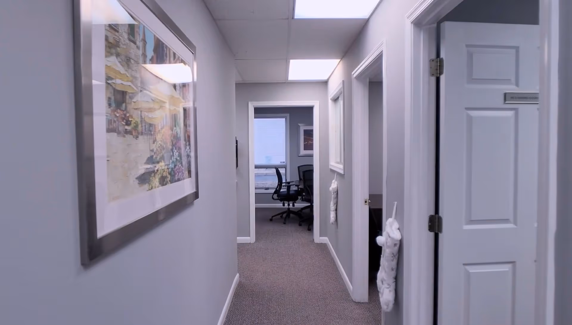 Narrow interior hallway at Aldrich Care Solutions with framed art and a distant office.