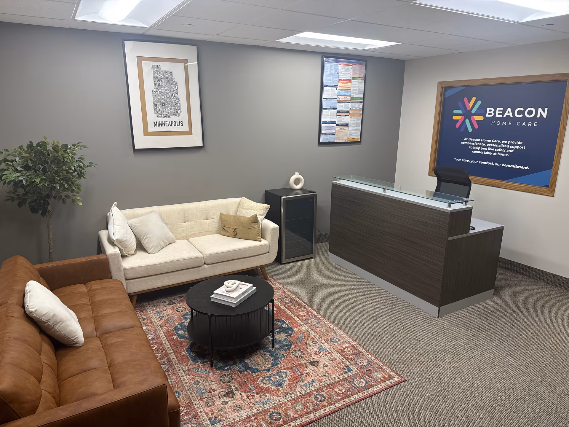 Reception lobby with sofa, chairs, coffee table, plant, and Beacon Home Care sign.