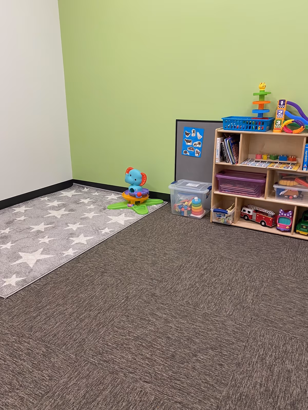 Bright green-walled playroom corner with toy shelf, plastic toys, and star-patterned rug.