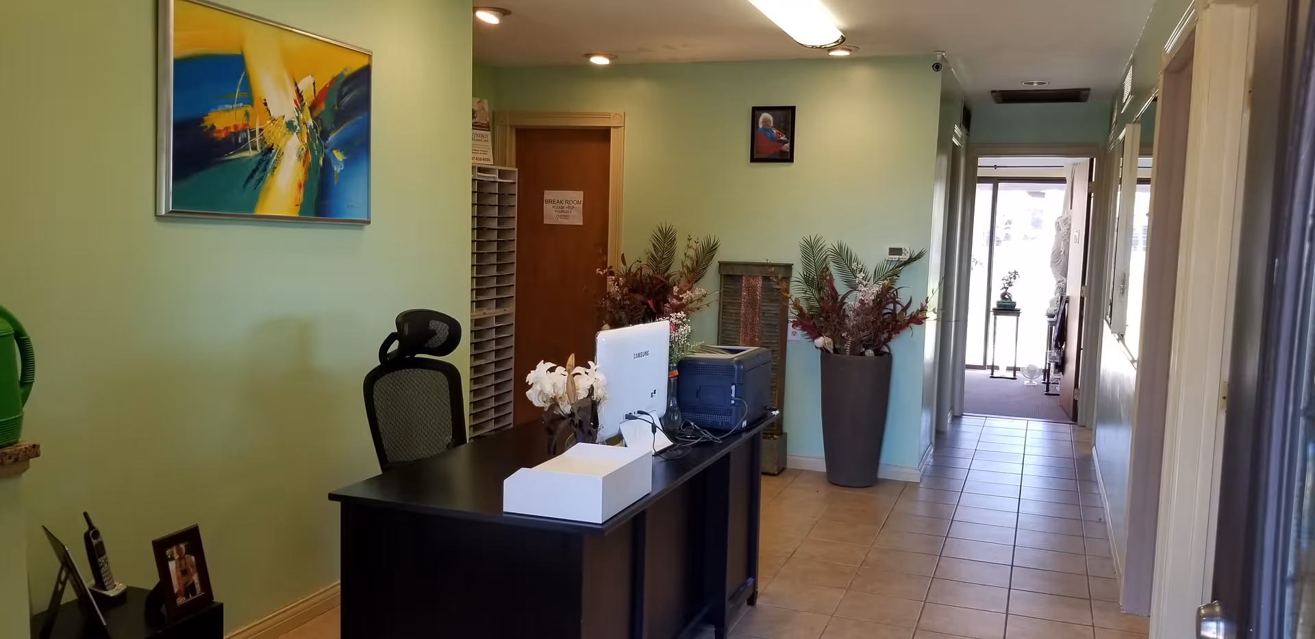 Reception desk in a mint-green hallway with plants and office equipment.