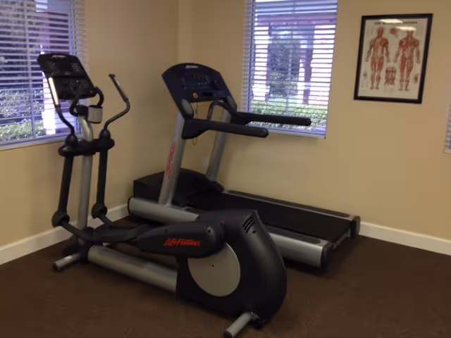 Two treadmills and a stationary bike in a small beige exercise room.