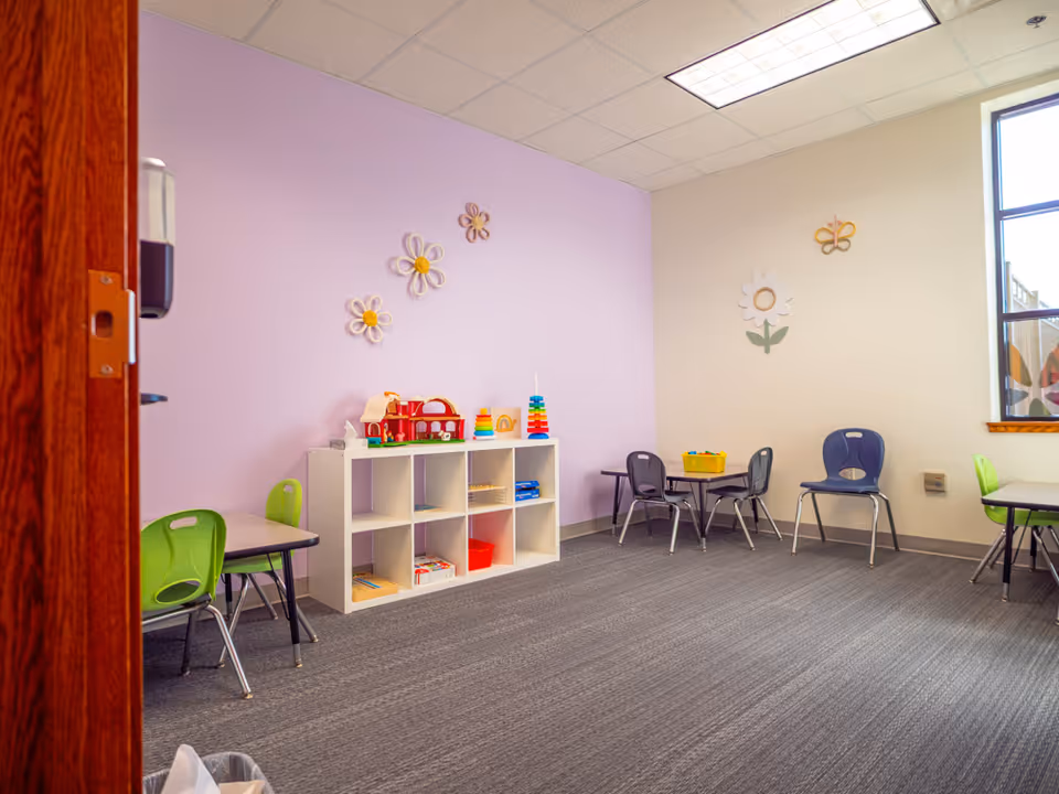 Bright interior playroom with purple walls, storage cubbies, toys, and small tables.
