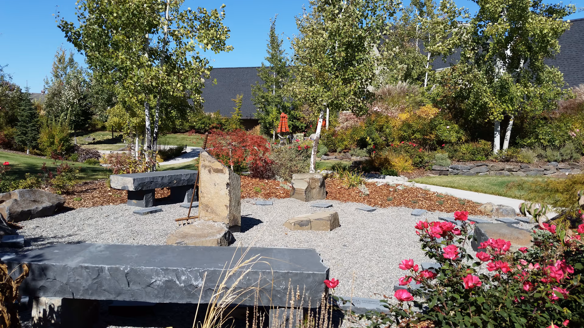 Outdoor garden at a hospice facility with stone benches, rocks, and blooming shrubs.